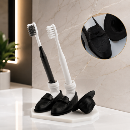 Two toothbrushes with black and white bristles, placed inside black loafers on a marble surface.