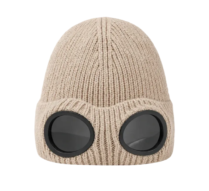 A beige ribbed knit beanie hat with two large round black goggles attached on the front, shown against a plain white background.