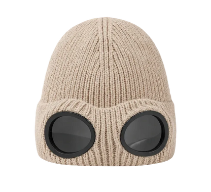 A beige ribbed knit beanie hat with two large round black goggles attached on the front, shown against a plain white background.